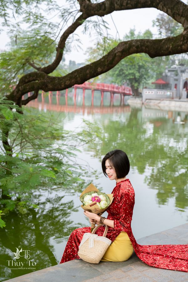 Áo dài đỏ ôm sen bên Hồ Gươm, cầu Thê Húc phía sau — Thúy Tô Studio