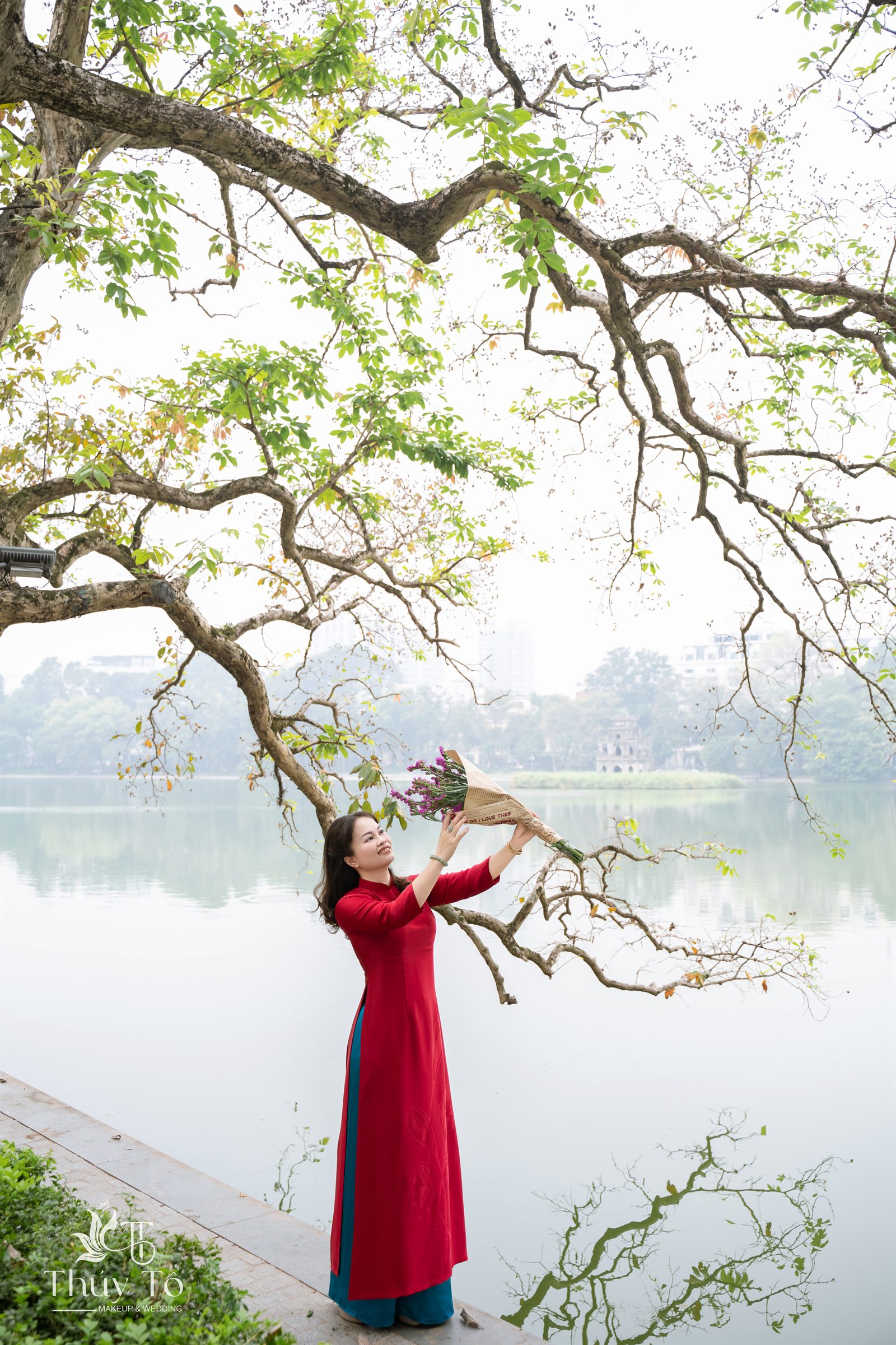 Cô gái mặc áo dài đỏ đứng dưới tán cây cổ thụ bên Hồ Gươm, ảnh do Thúy Tô Studio chụp